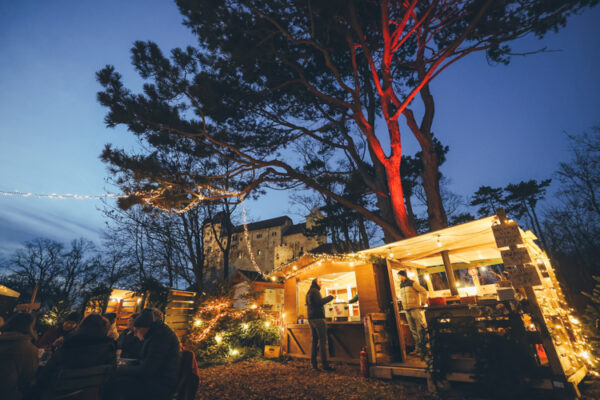 Beleuchteter Weihnachtsmarkt mit Baum vor Burg in der blauen Stunde