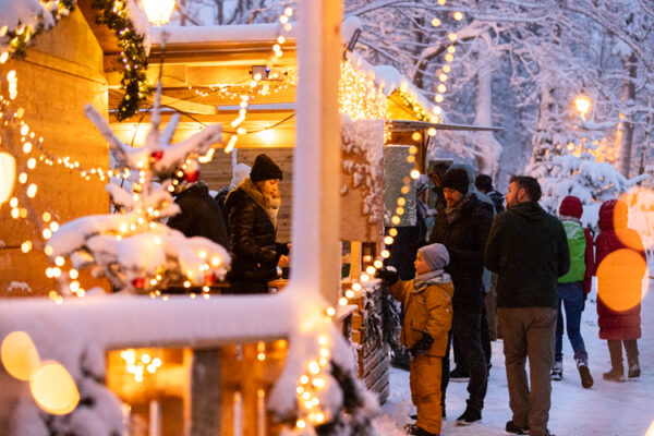 Weihnachtsmarkt mit Hütte, Lichter und Schnee und einem kleinen Jungen