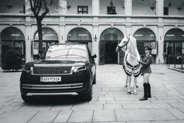 Elevin mit einem Pferd der Spanischen Hofreitschule im Hof neben einem parkenden Range Rover